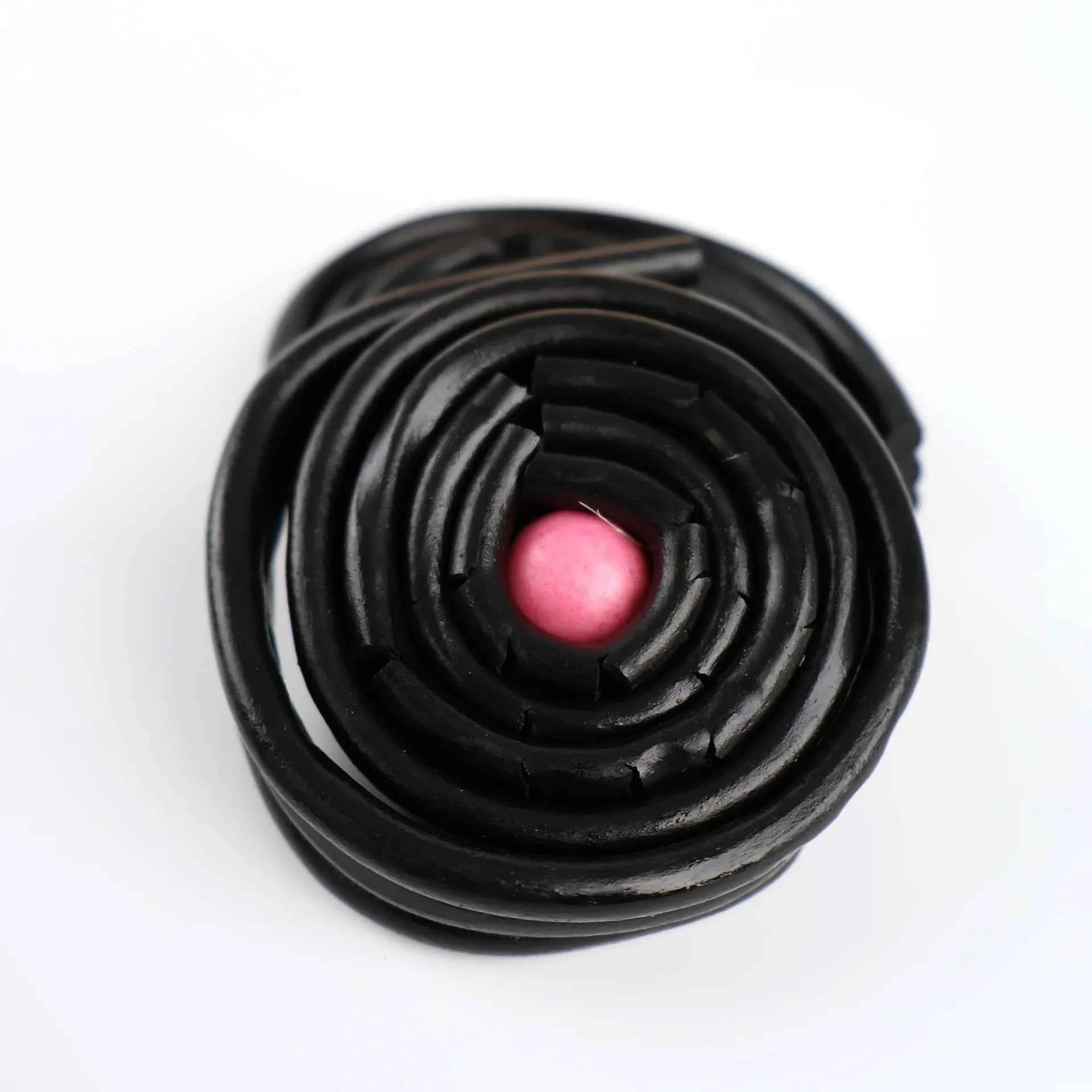 Gros plan sur un rouleau de réglisse noire avec une bille de gum rose.