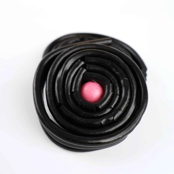 Gros plan sur un rouleau de réglisse noire avec une bille de gum rose.