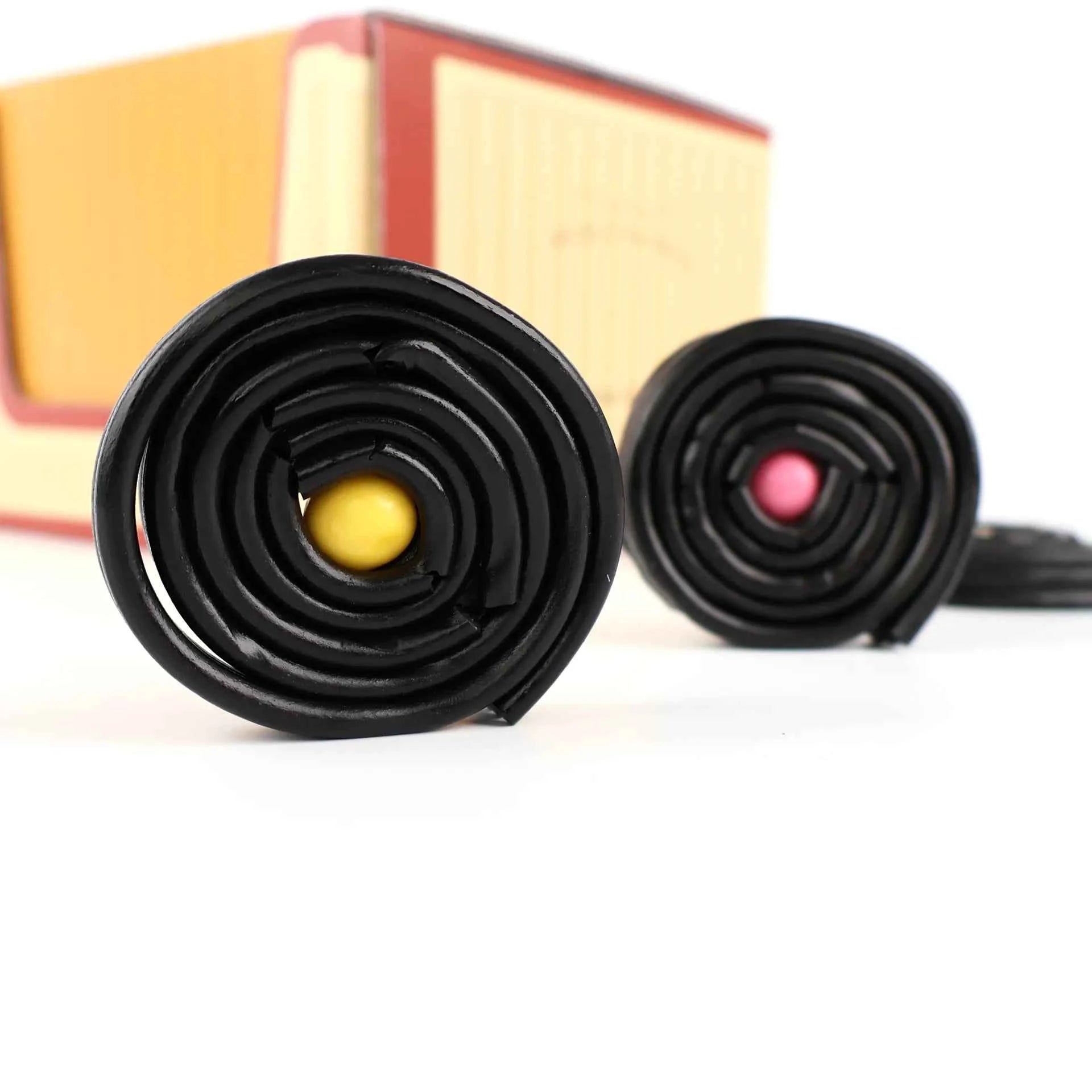 Deux rouleaux de réglisse noire posés devant leur boîte.