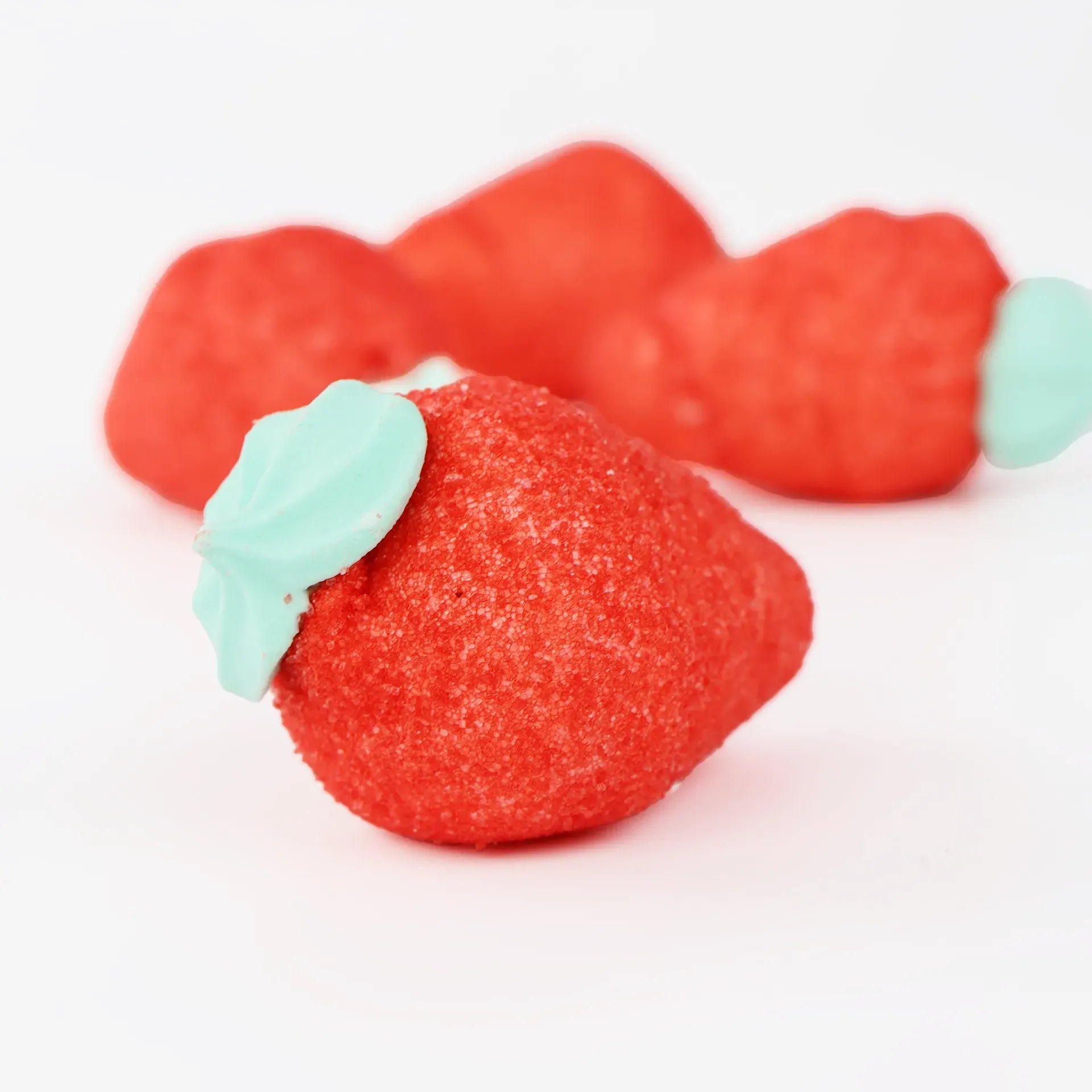 Fraises gélifiées rouges et verts posés sur un fond blanc.