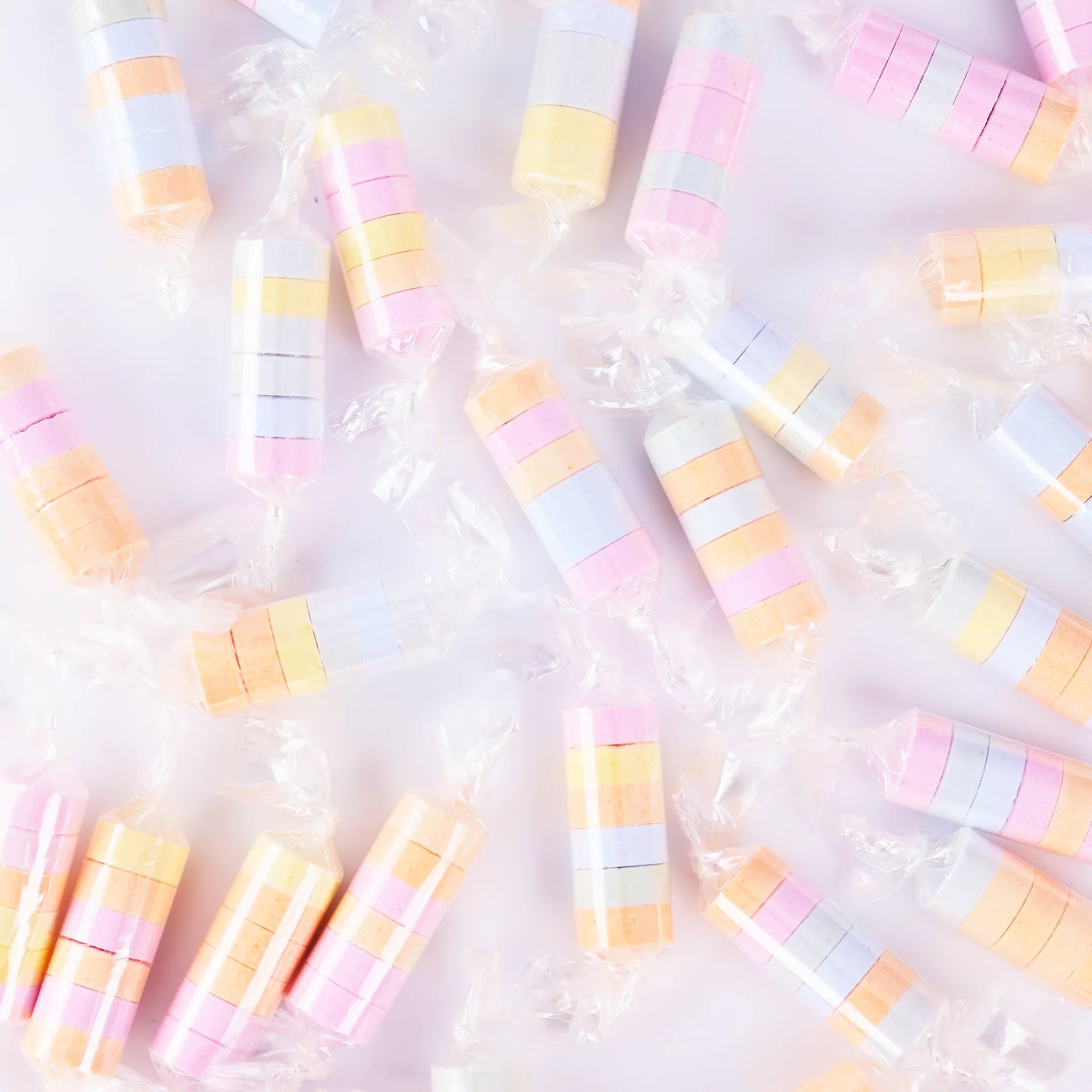 Gros plan sur les rouleaux de bonbons dextrose multicolores (bleu, jaune, orange, rose) dans leurs emballages transparents.